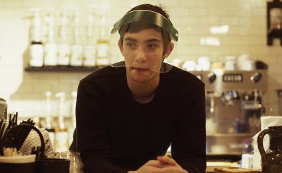 Юноша в защитом экране за стойкой в кафе беседует с девушкой