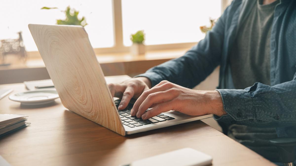 Мужчина в синей рубашке за столом печатает на ноутбуке