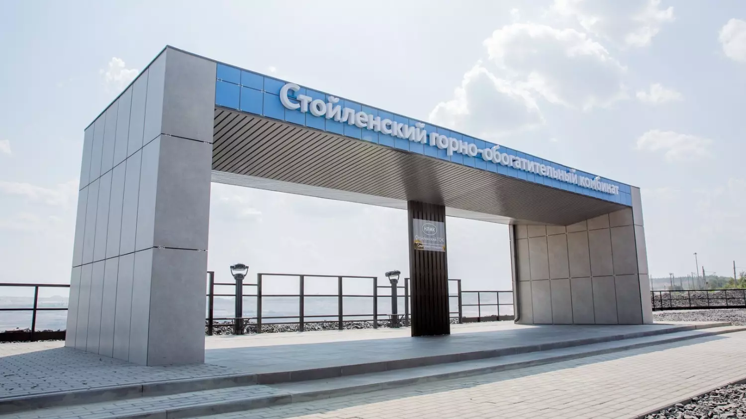 Панорамный вид на огромный карьер с техникой и смотровой площадкой на переднем плане.