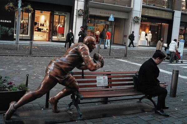 Мужчина сидит на скамейке рядом со статуей в стиле регби, Япония. - Sputnik Грузия