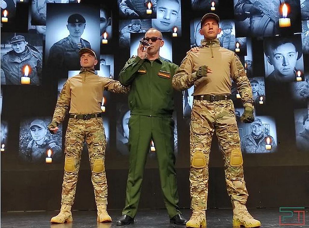 На сцене - 3 человека в форме, один из них - в тёмных очках
