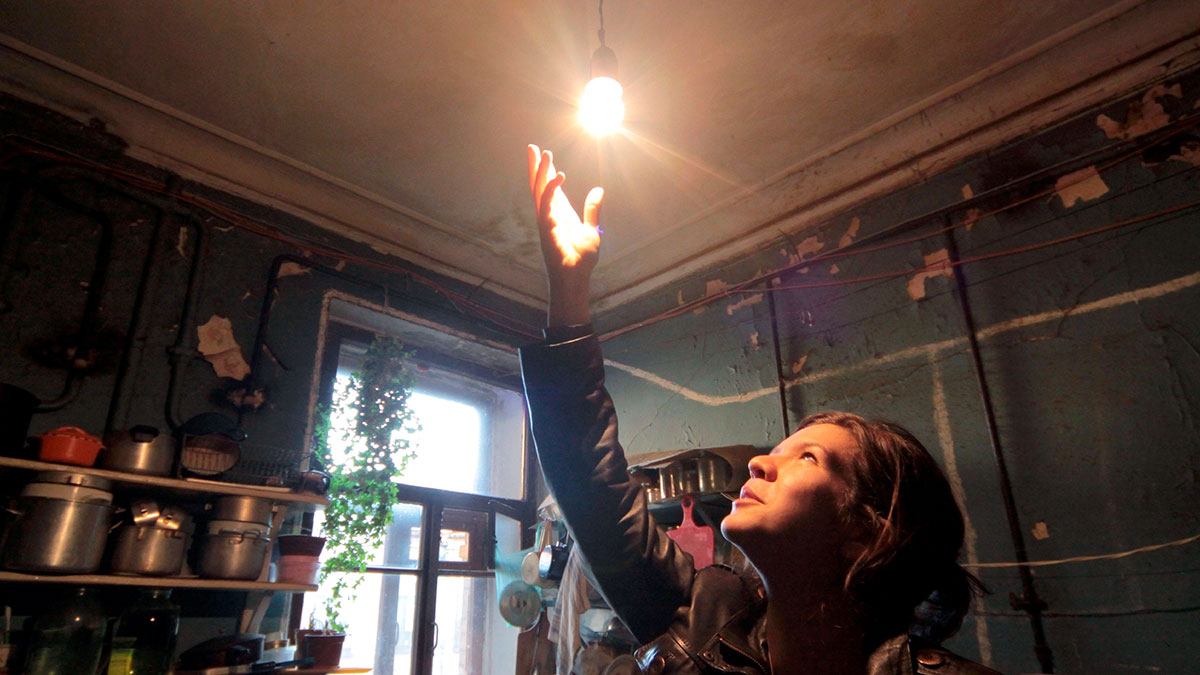 Девушка протягивает руку к электрической лампочке