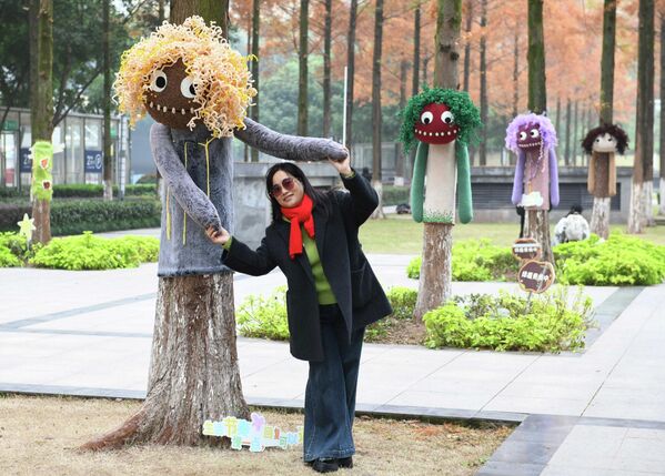 Житель города позирует для фотографии на фоне деревьев, украшенных разноцветными свитерами в Чунцине, Китай. - Sputnik Грузия