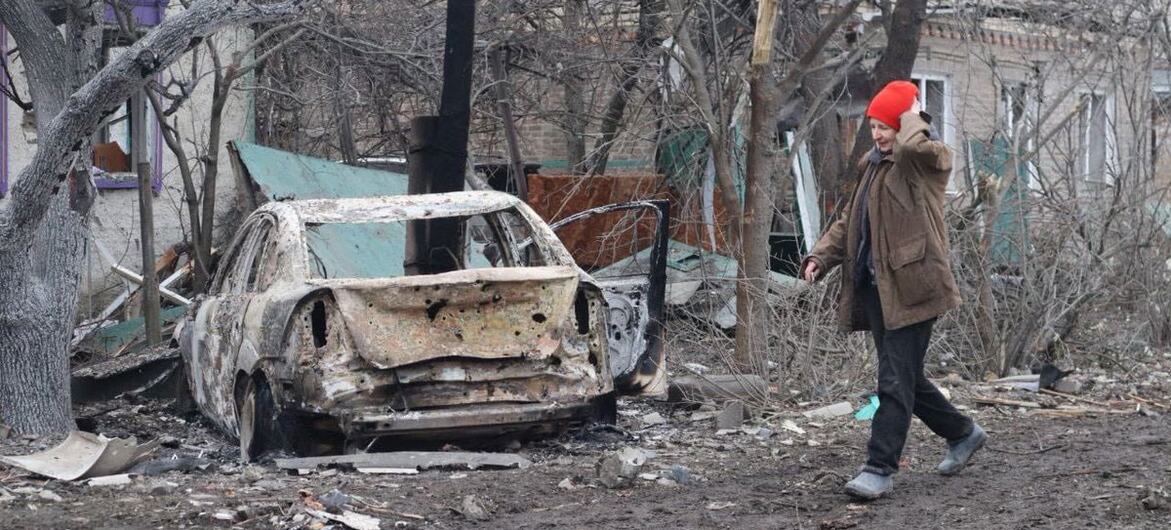 Женщина в красной шляпе проходит мимо сгоревшей машины и разрушенных зданий в Краматорске, Украина, после нападения.