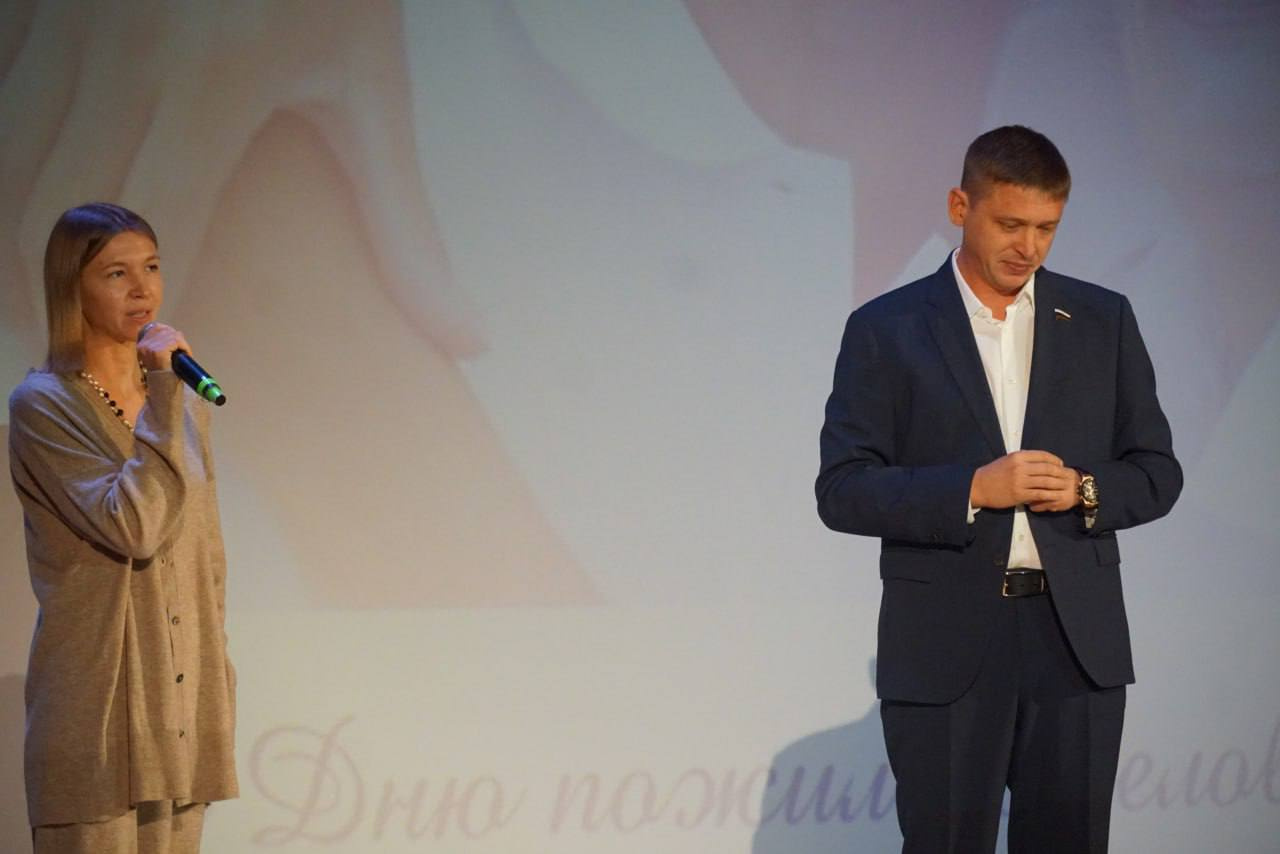 Антон Красноштанов стоит на сцене во время концерта ко Дню пожилого человека, из-под рукава выглядывают часы