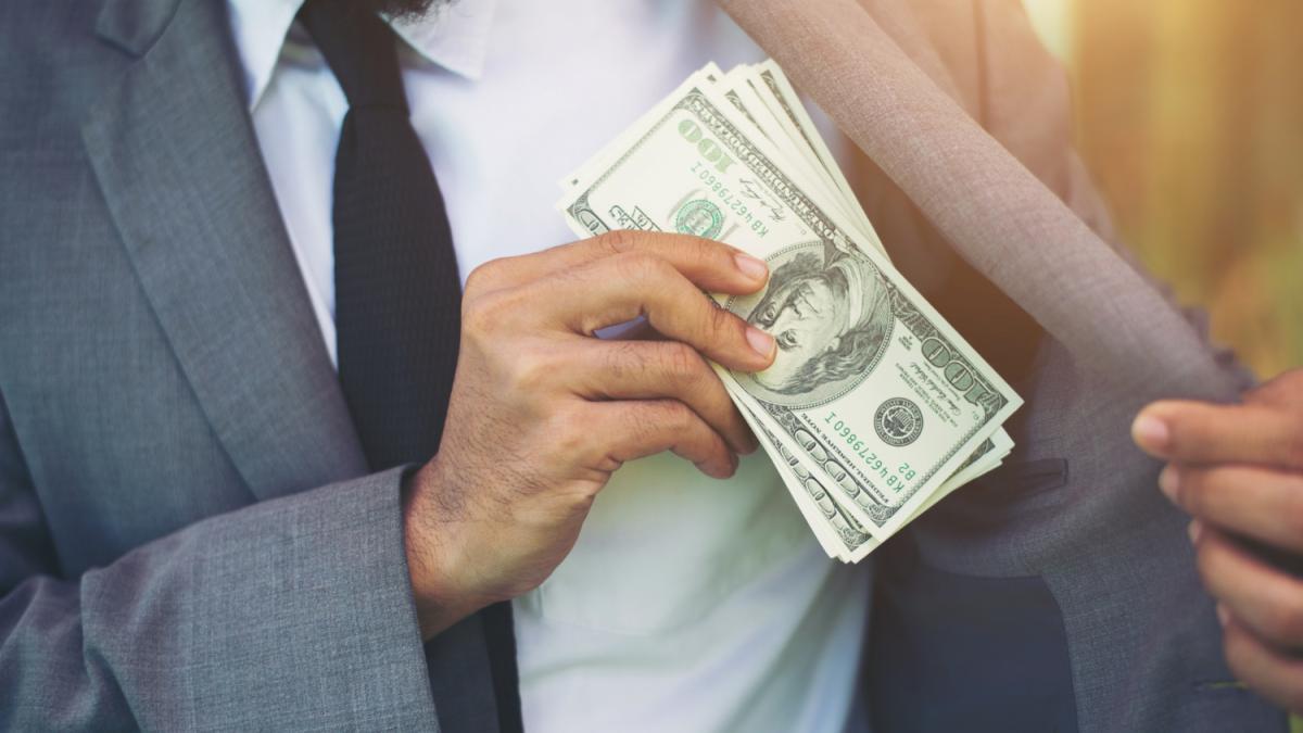 Мужчина кладёт доллары в карман пиджака