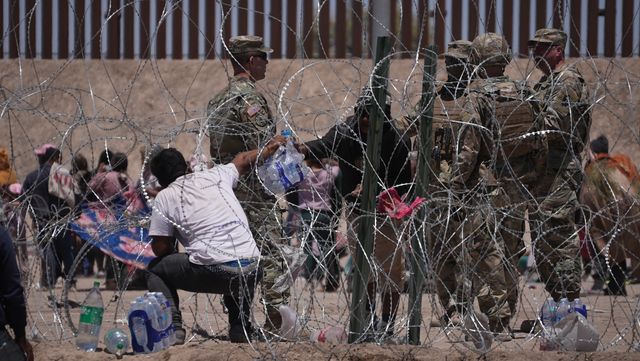 Мигрант из Венесуэлы передает питьевую воду человеку через забор из колючей проволоки на границе Мексики и США