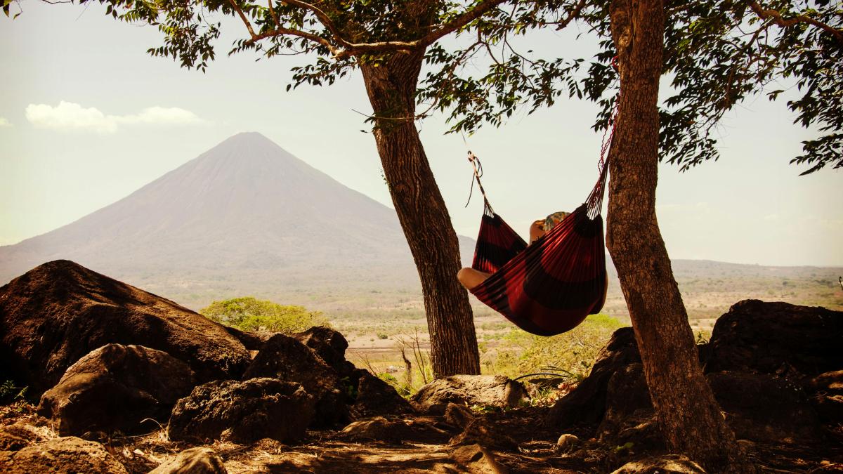 Person Lying on Black and Red Hammock Beside Mountain Under White Cloudy Sky during Daytime