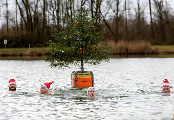 Мужчина и женщина в шапках Санта-Клауса купаются в озере, Германия. - Sputnik Грузия