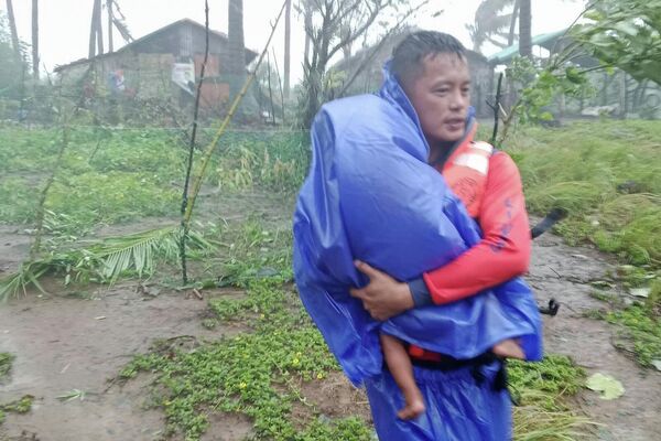 На этом фото, предоставленном береговой охраной, спасатель эвакуирует ребенка в безопасное место после супертайфуна Рагаса на севере Филиппин - Sputnik Абхазия