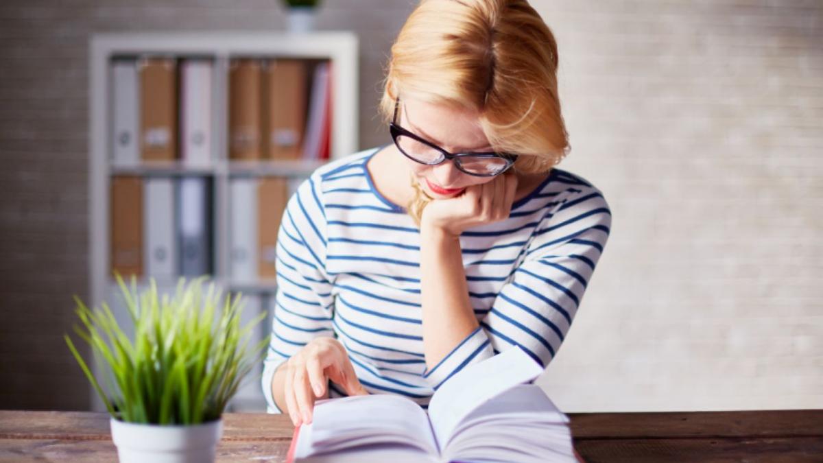 Девушка сидит за деревянным столом и читает книгу
