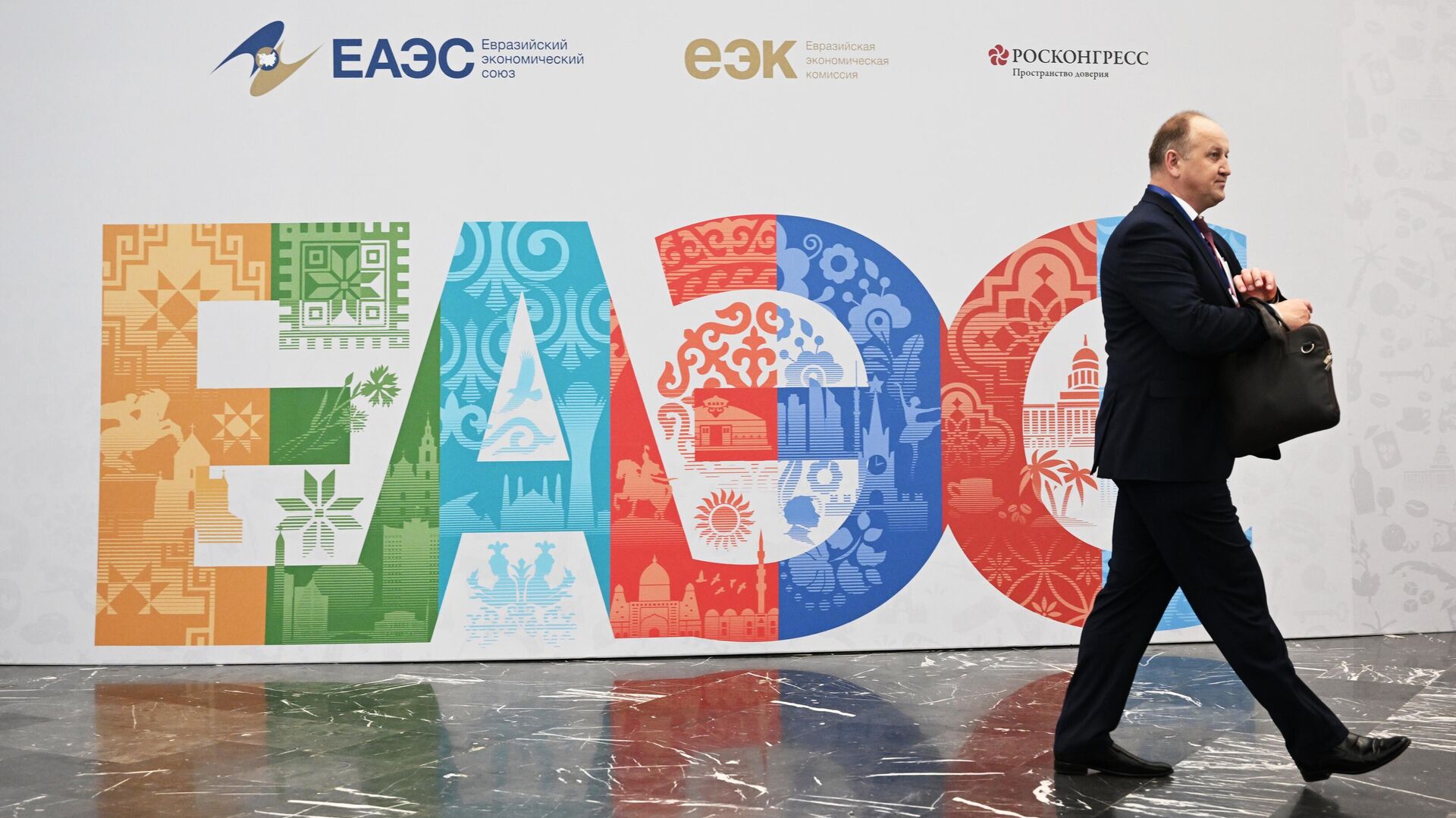  Участники проходят рядом со стендом с символикой Евразийского экономического форума - Sputnik Азербайджан, 1920, 16.04.2024